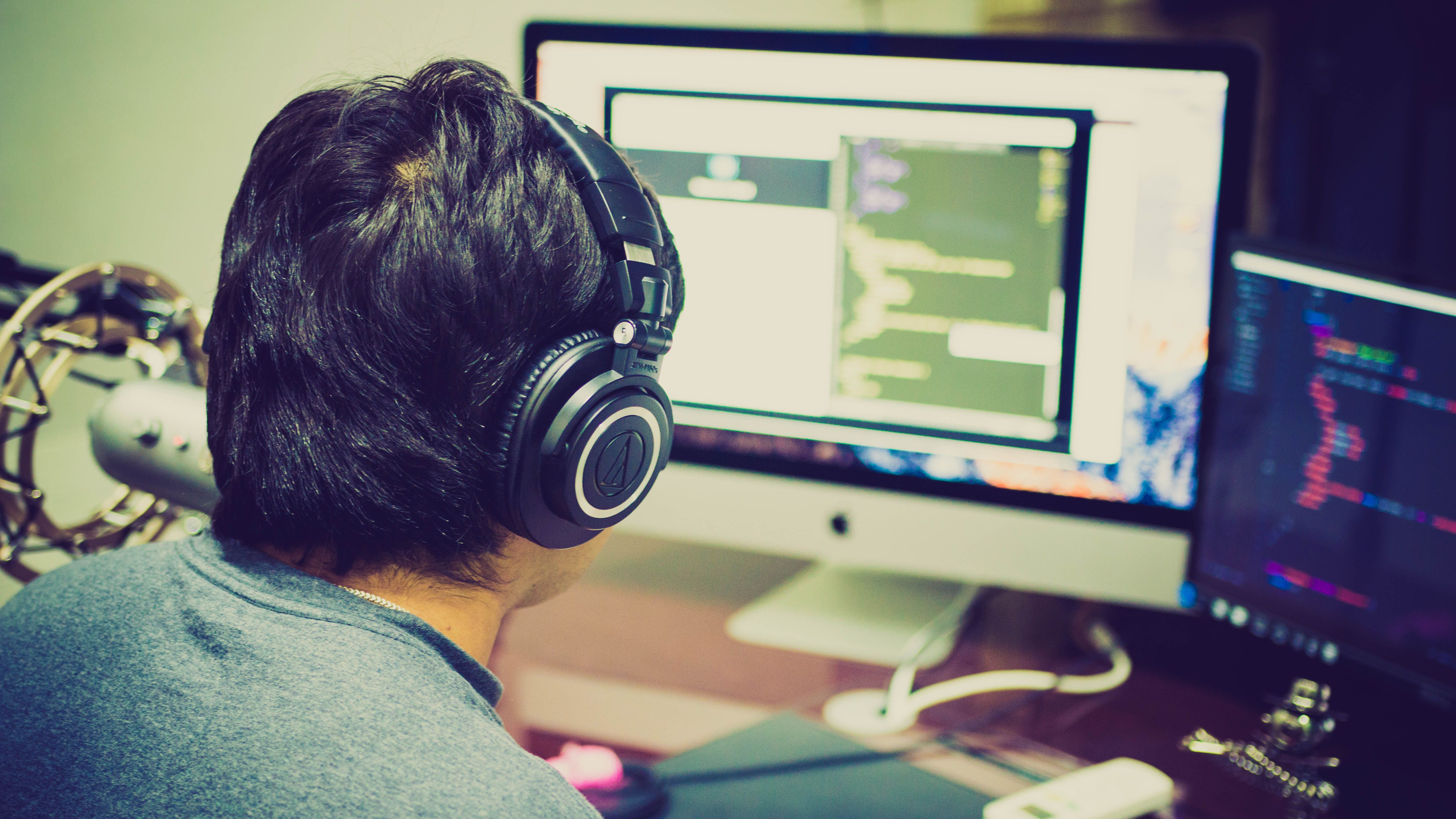 A programmer with headphones coding at a dual-monitor computer setup