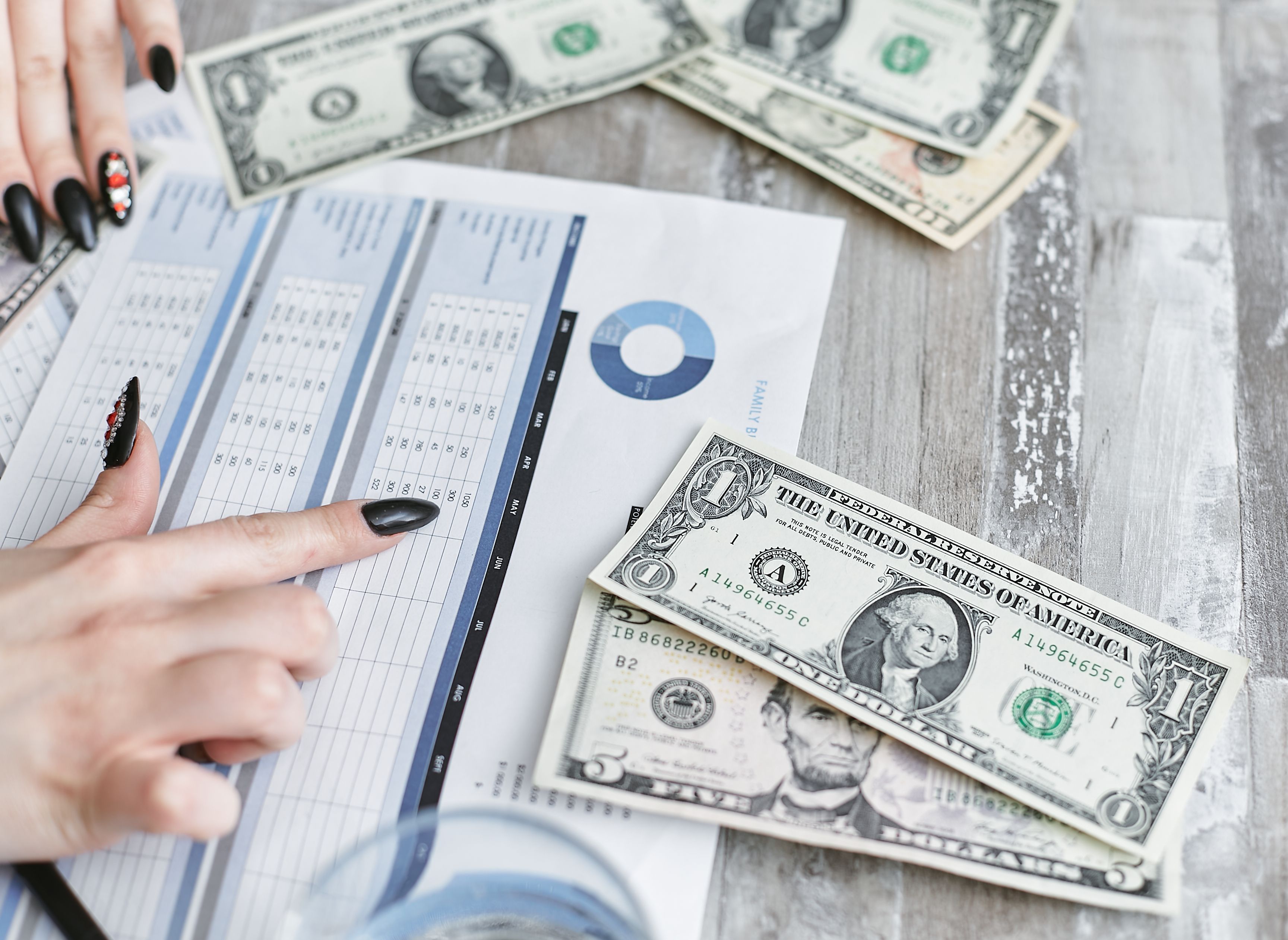 Close-up of hands analyzing a financial document with US dollar bills on the table
