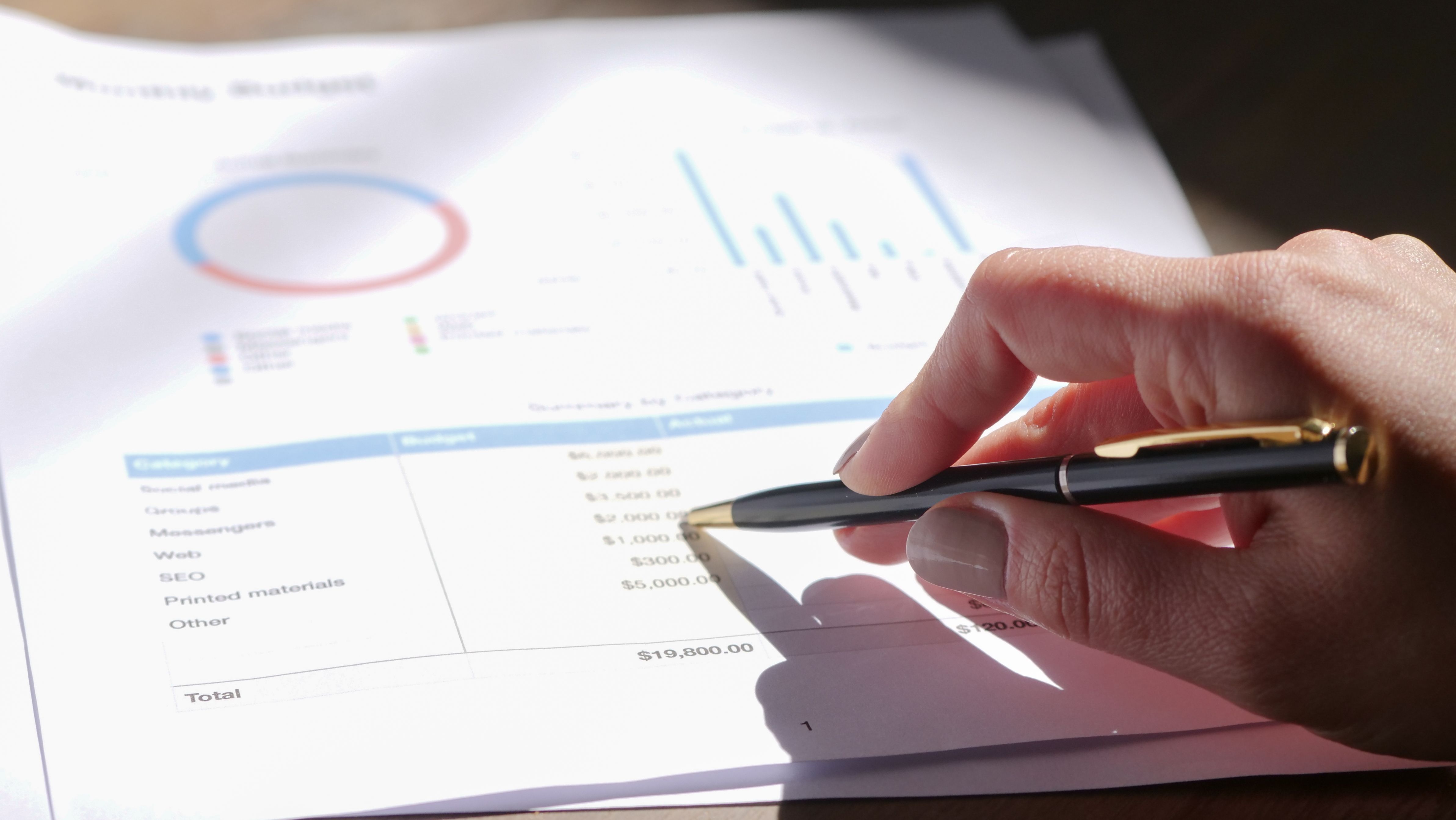 Hand holding a pen while analyzing a budget with charts and graph paper