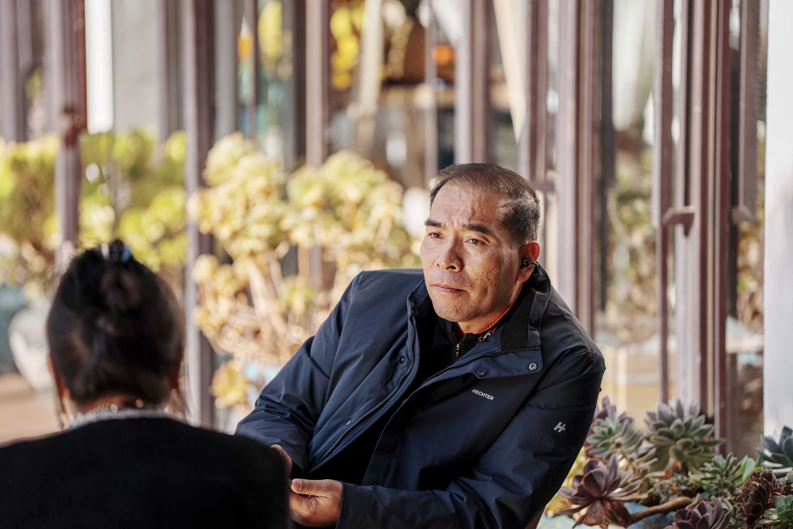 Two adults engaged in a relaxed conversation at a sunny outdoor cafe, suggesting the first steps toward trust with a stranger.