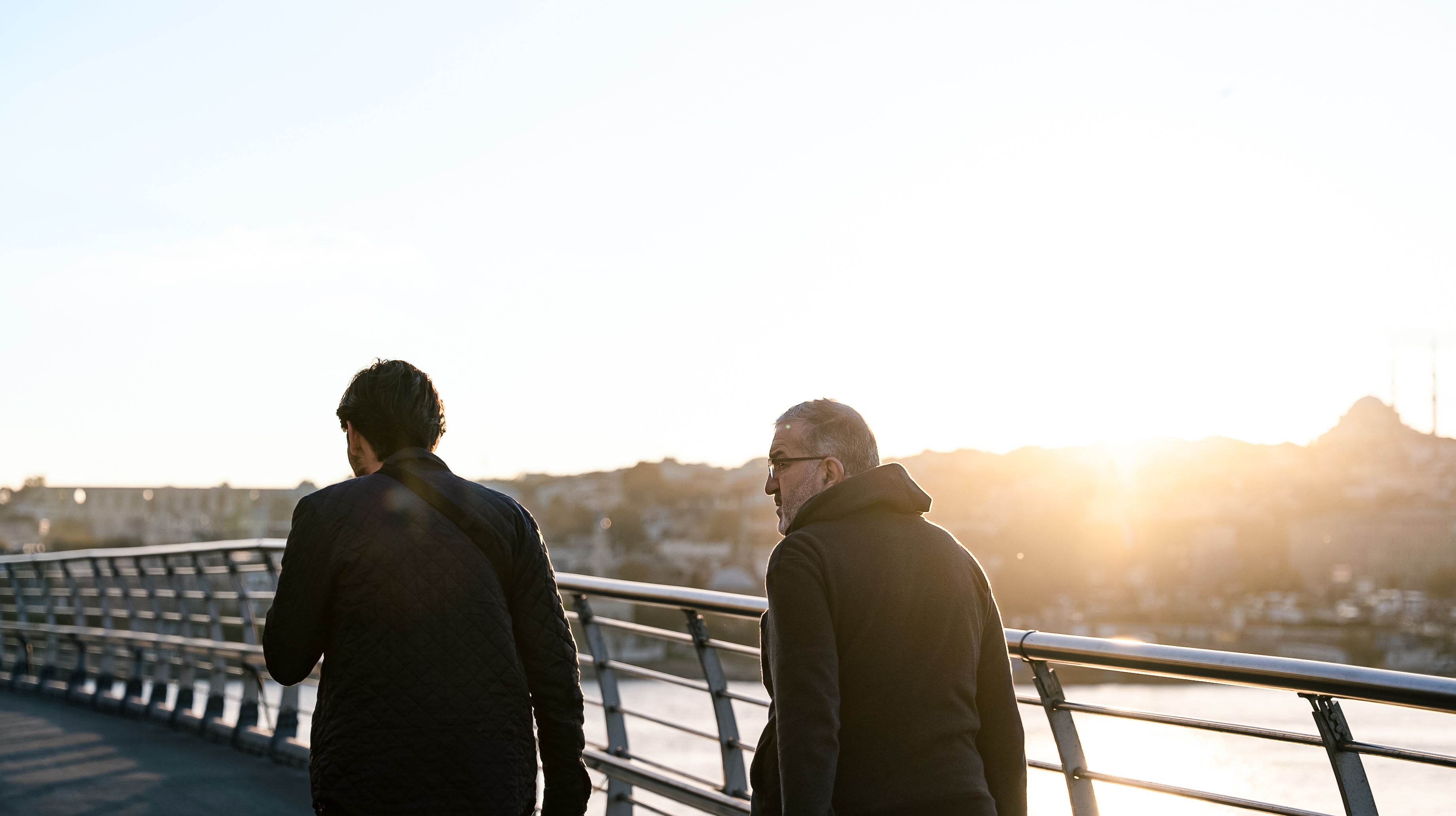 Two men talking while walking across a bridge at sunset, illustrating connection developing between unfamiliar people.