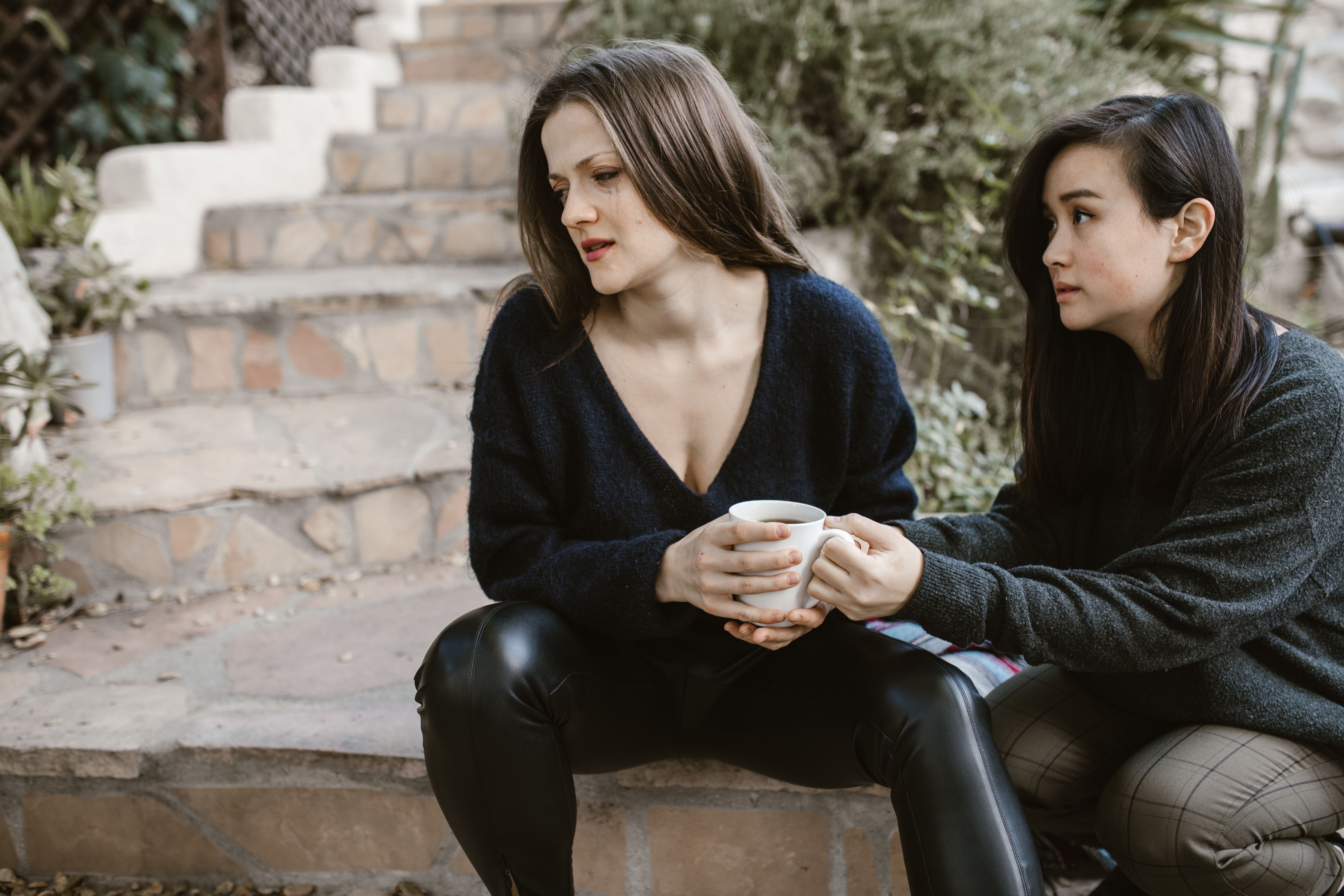 One woman offering comfort to another on outdoor steps, representing empathy and the safety needed for vulnerability.